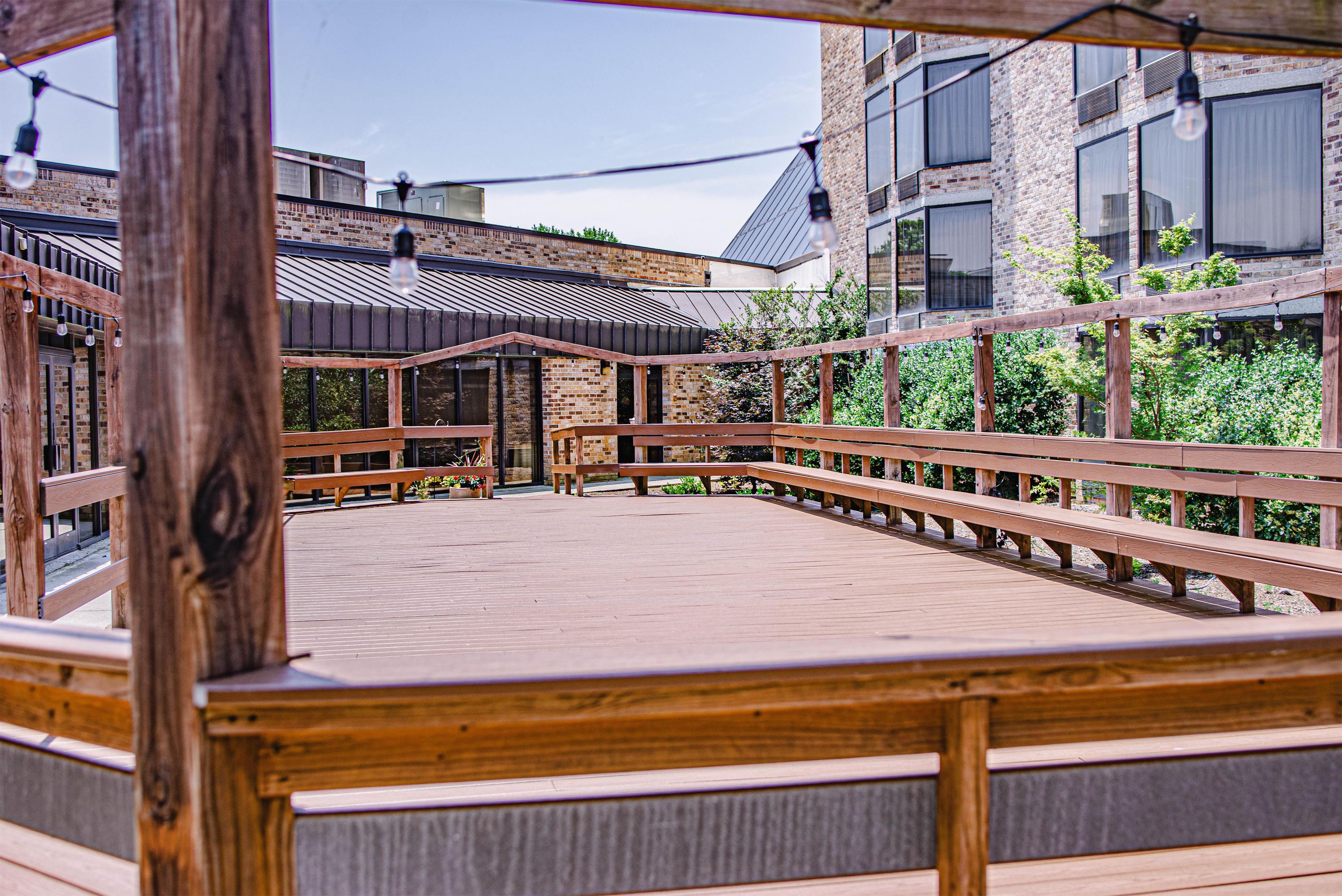 A wooden deck with benches, surrounded by brick buildings and greenery.