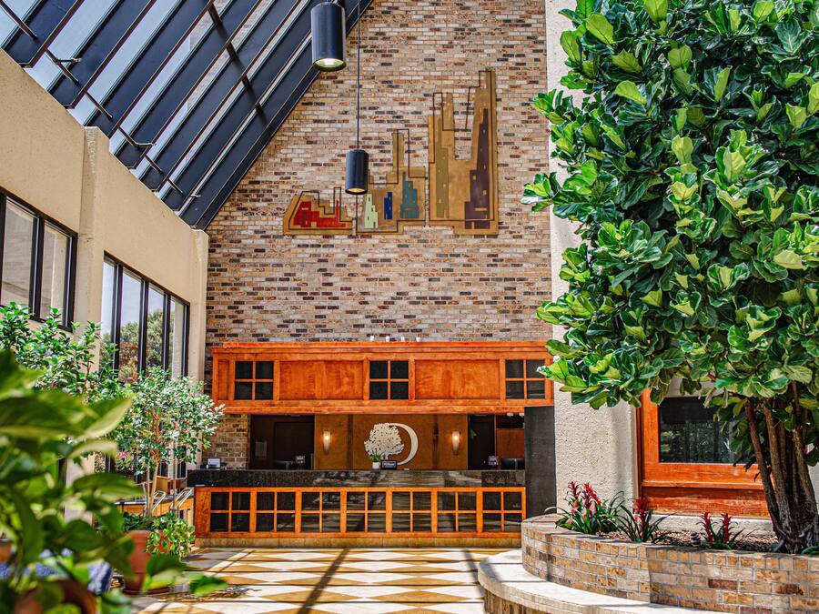 A hotel lobby with a brick wall, a wooden reception desk, and a large tree.