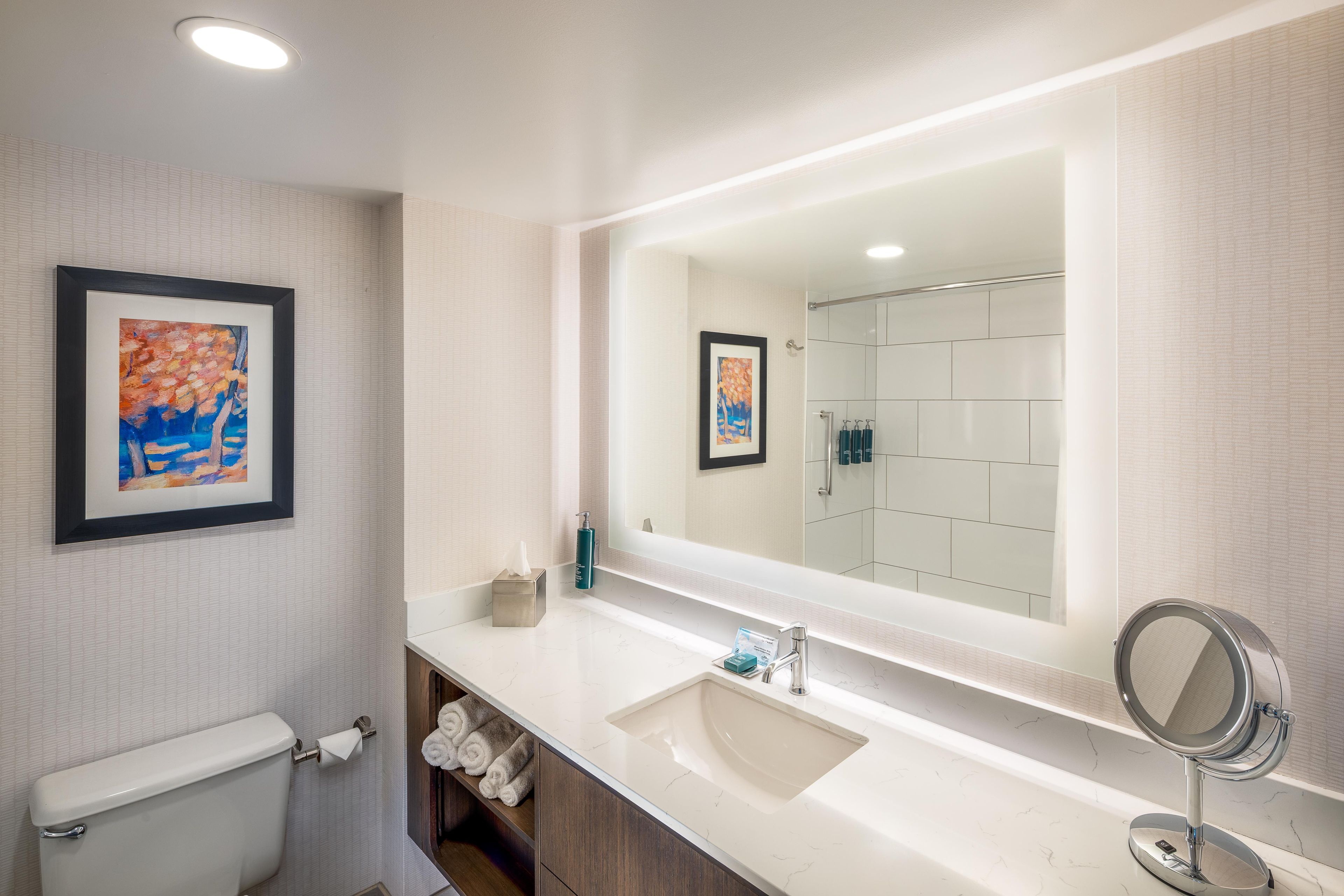 Een moderne badkamer met een grote spiegel, witte tegels, een toilet en een handdoekhouder.