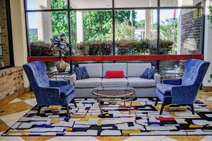 A modern lounge area with a grey sofa, two blue armchairs, a glass coffee table, and a patterned rug. - DoubleTree by Hilton Hotel Oak Ridge - Knoxville (Oak Ridge)