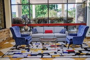 Un área de descanso moderna con un sofá gris, dos sillones azules, una mesa de centro de vidrio y una alfombra estampada.