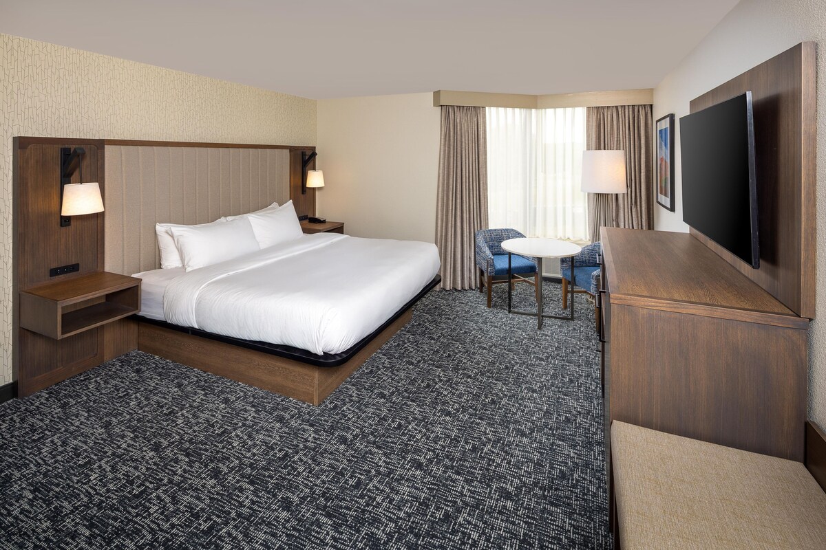 A hotel room with a large bed, a desk with a chair, a TV, and a window with curtains.