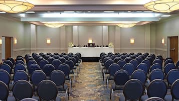 Ein Konferenzraum mit Stuhlreihen, die zu einem Rednerpult blicken, einem gemusterten Teppich und Wandleuchten.