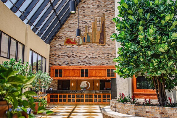 A lobby with a brick wall, wooden reception desk, and a large tree.