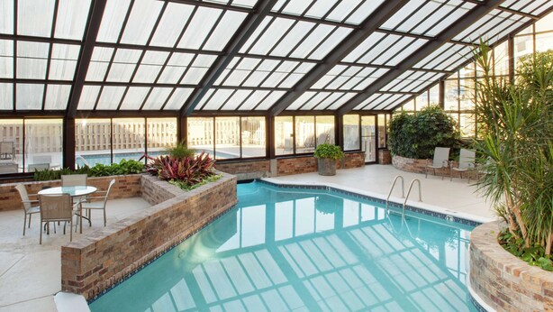An indoor swimming pool with a glass ceiling, surrounded by brick walls and potted plants. - DoubleTree by Hilton Hotel Oak Ridge - Knoxville (Oak Ridge)