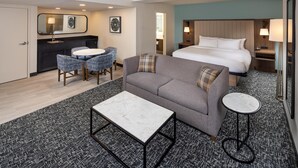 A hotel room with a bed, a sofa, a round table, a small round table, a desk, a chair, a mirror, and a wall-mounted lamp. - DoubleTree by Hilton Hotel Oak Ridge - Knoxville (Oak Ridge)