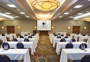 A conference room with multiple tables, chairs, and a large screen displaying the DoubleTree by Hilton logo. - DoubleTree by Hilton Hotel Oak Ridge - Knoxville (Oak Ridge)