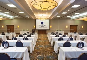 Un salón de conferencias con varias mesas, sillas y una gran pantalla que muestra el logotipo de DoubleTree by Hilton.