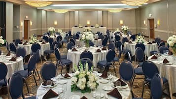 A banquet hall with round tables set for dining, each with white tablecloths, dark blue chairs, and floral centerpieces.