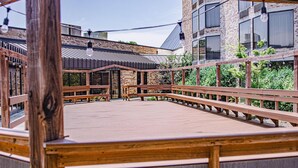 An outdoor wooden deck with benches, surrounded by brick buildings and greenery. - DoubleTree by Hilton Hotel Oak Ridge - Knoxville (Oak Ridge)