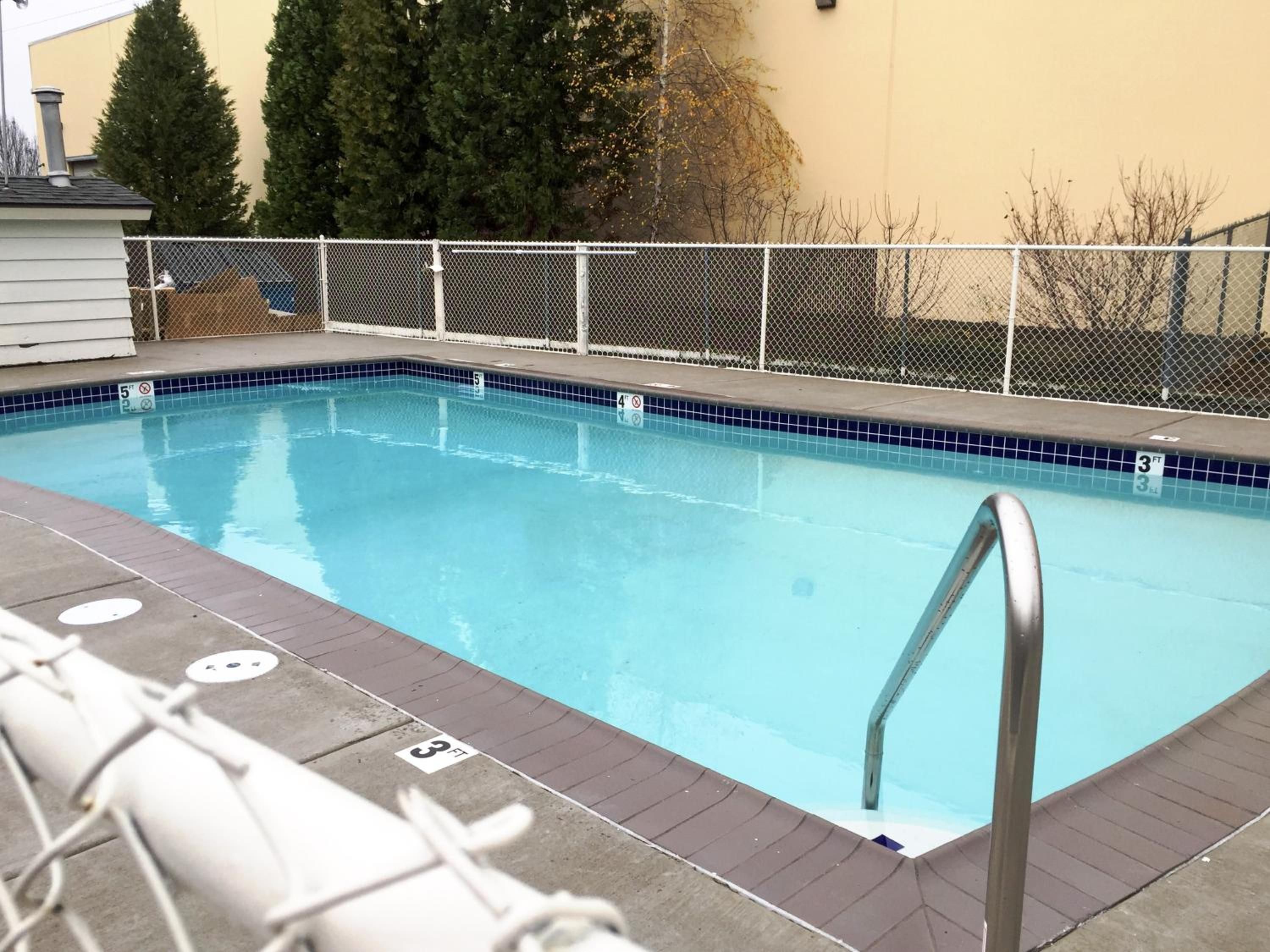 A rectangular swimming pool with a metal ladder, surrounded by a white fence, and a tiled edge.