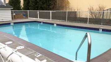 A rectangular swimming pool with a metal ladder, surrounded by a white fence, and a tiled edge.