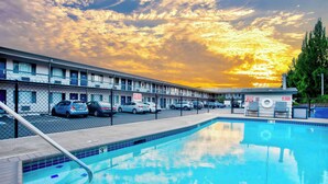 Un motel avec une piscine, des voitures garées devant et un ciel au coucher du soleil.