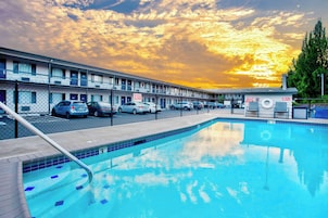 A motel with a swimming pool, cars parked in front, and a sunset sky.