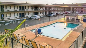 A motel with a swimming pool, outdoor seating, and a parking lot with cars.