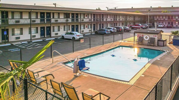 Un motel con piscina, zona de estar exterior y aparcamiento con coches.