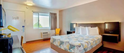 A hotel room with a bed, a desk with a lamp, a chair, a TV, and a window with curtains.