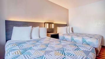 A hotel room with two beds, each with a patterned bedspread, a nightstand with a lamp, and a wooden floor.