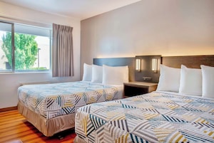 A hotel room with two beds, a large window with curtains, and a nightstand with a lamp.
