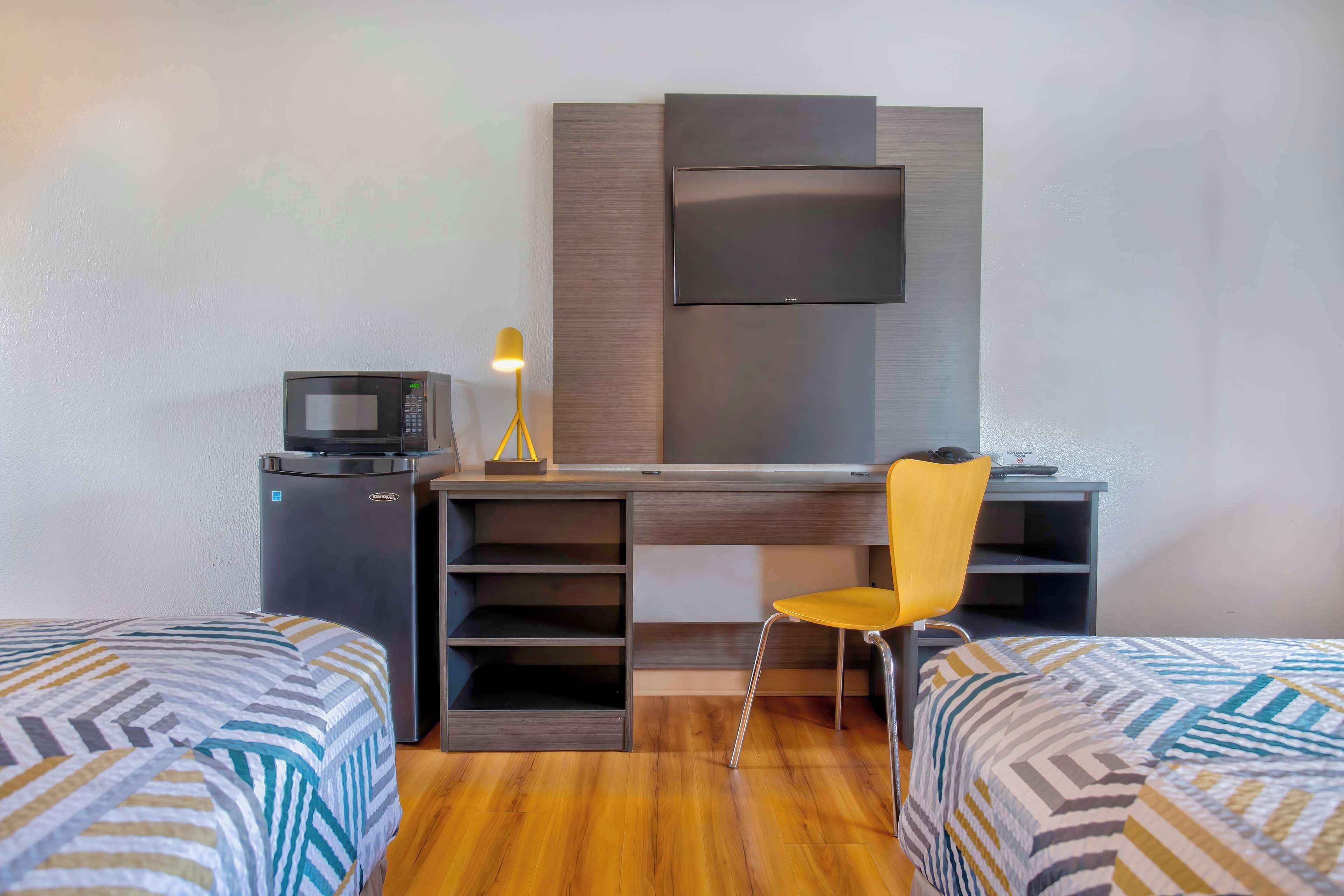 Habitación de hotel con cama, escritorio, silla, televisión, microondas y lámpara.