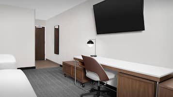 Une chambre d’hôtel comprenant un lit, un bureau avec une chaise, un téléviseur à écran plat fixé au mur et une armoire en bois.