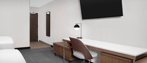 A hotel room with a bed, a desk with a chair, a flat-screen TV mounted on the wall, and a wooden cabinet.