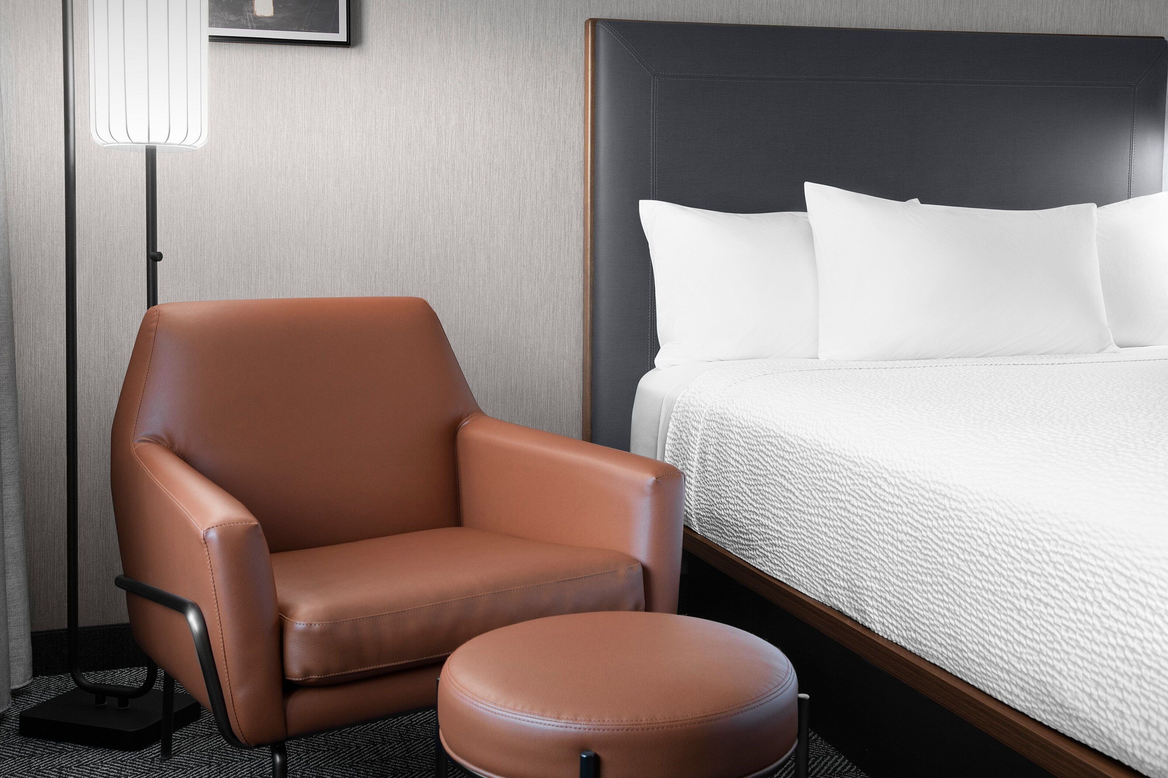 Una habitación de hotel con una cama, un sillón de cuero marrón y un reposapiés a juego.