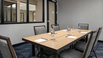 Ein Konferenzraum mit einem langen Tisch, sechs Stühlen und einem großen Spiegel an der Wand.