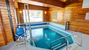An indoor swimming pool with a wooden interior, a blue chair, and a ladder leading into the pool. - Country Inn & Suites by Radisson, Traverse City, MI (Traverse City)