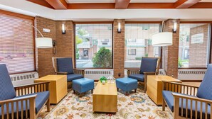 A room with a wooden ceiling, large windows with blinds, a central coffee table, and blue upholstered chairs. - Country Inn & Suites by Radisson, Traverse City, MI (Traverse City)