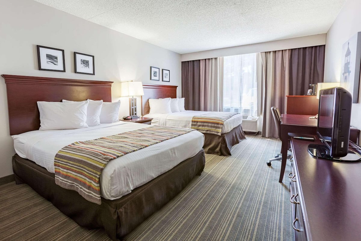 A hotel room with two beds, a desk, a chair, and a television.