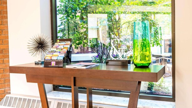 A wooden table with a travel guide, a decorative glass vase, and a starburst ornament near a window with a view of greenery and a building. - Country Inn & Suites by Radisson, Traverse City, MI (Traverse City)