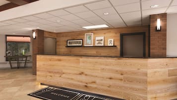 A reception desk with a wooden finish, framed artwork on the wall, and a welcome mat on the floor.