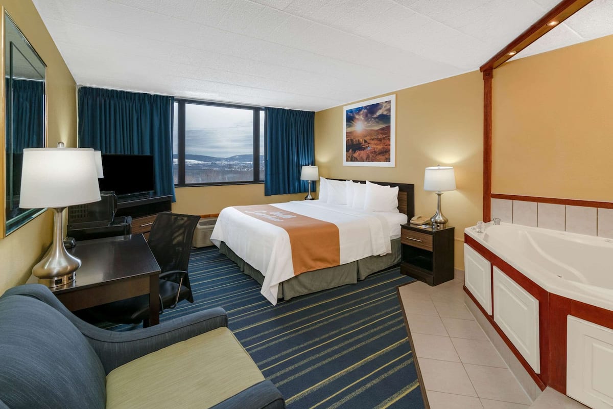 A hotel room with a bed, a desk, a TV, a sofa, a bathroom with a bathtub, and a city view.
