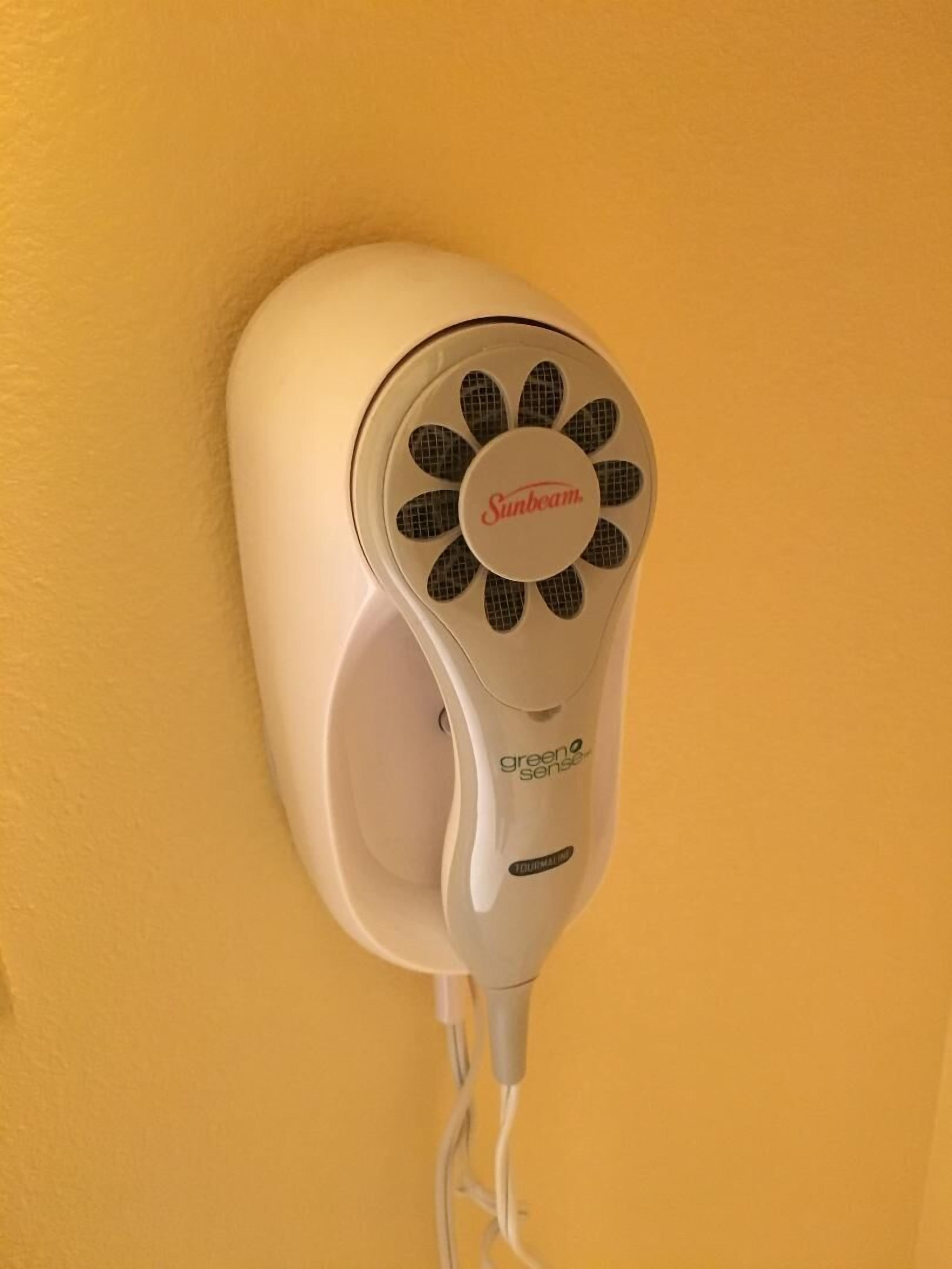 A Sunbeam hair dryer mounted on a yellow wall.