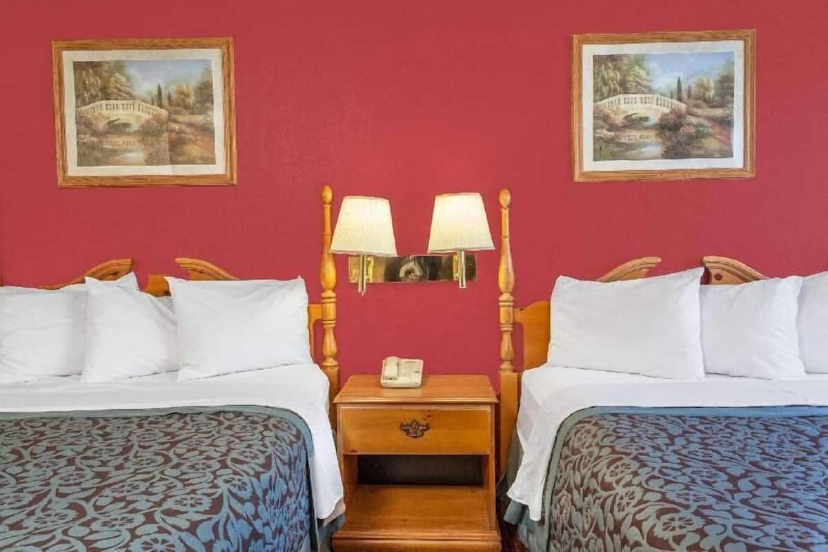 A hotel room with two beds, a nightstand with a lamp, and two framed pictures on the wall.