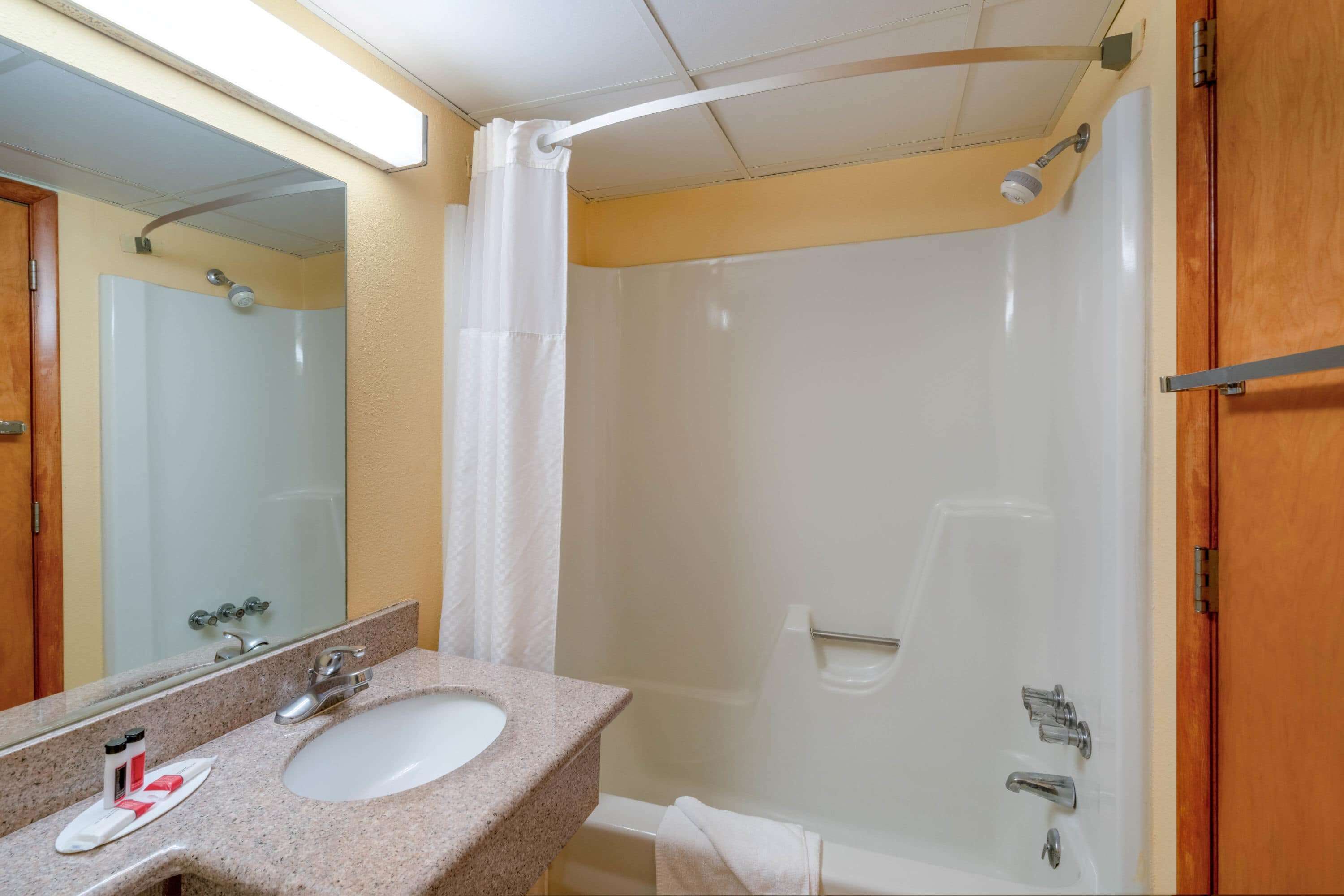 A bathroom with a sink, mirror, shower, and towel rack.