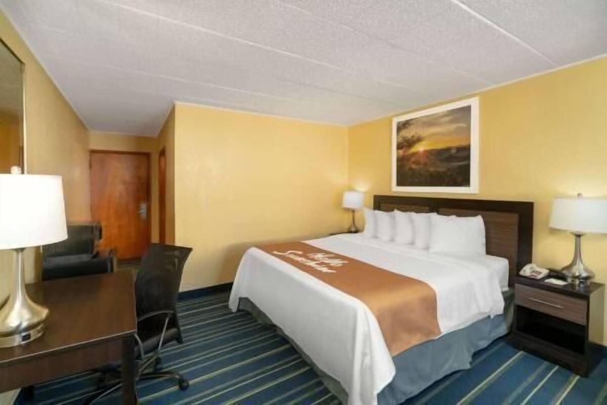 A hotel room with a bed, desk, chair, and a painting on the wall.