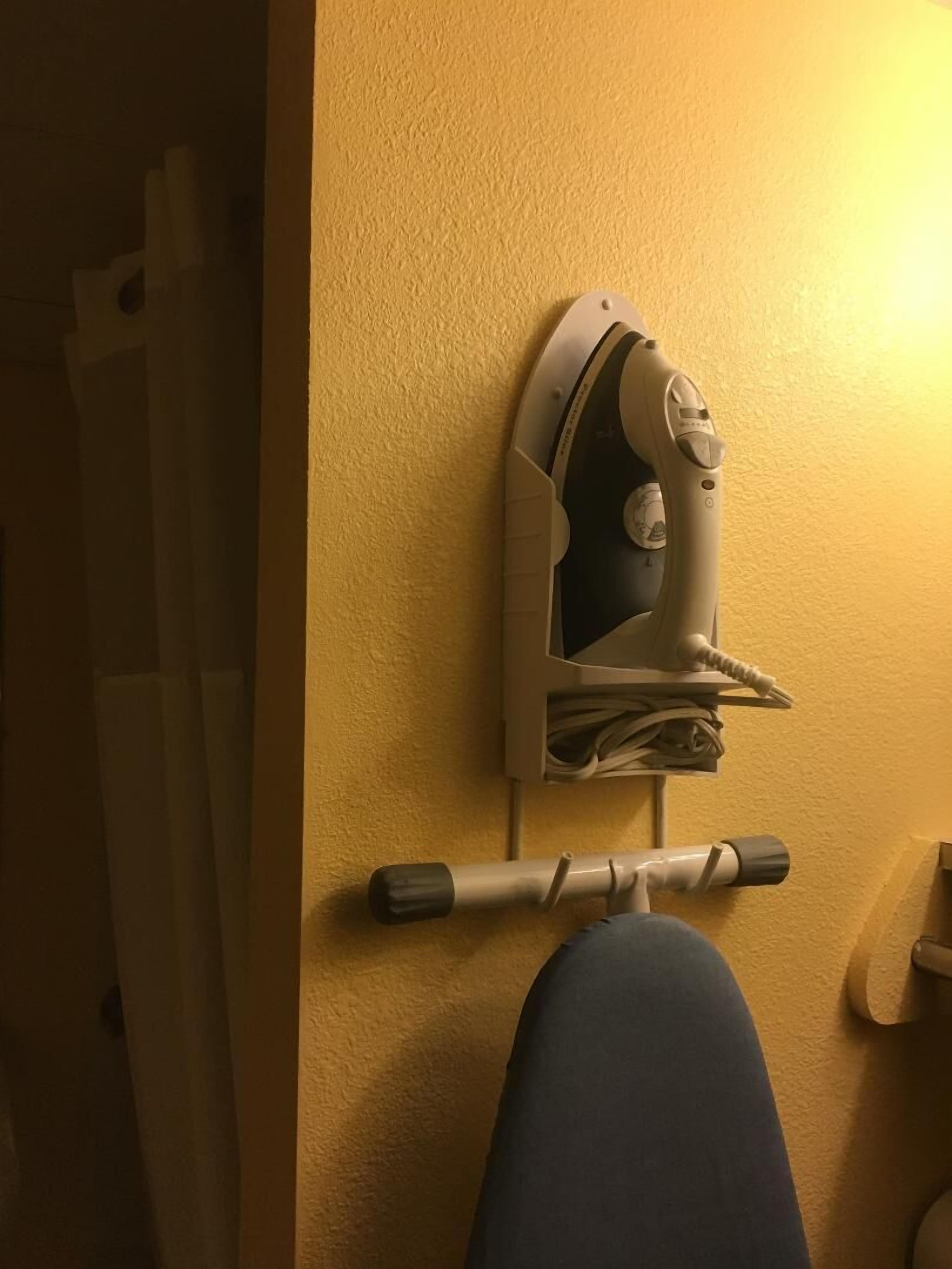 A wall-mounted ironing board with an iron, a curtain, and a wooden door.