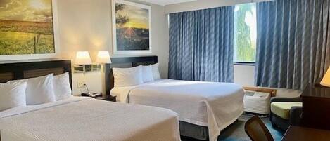 A hotel room with two beds, a desk, a chair, and a large window with curtains.