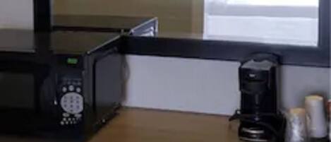 A hotel room with a large mirror, a microwave, a coffee maker, and a window with curtains.