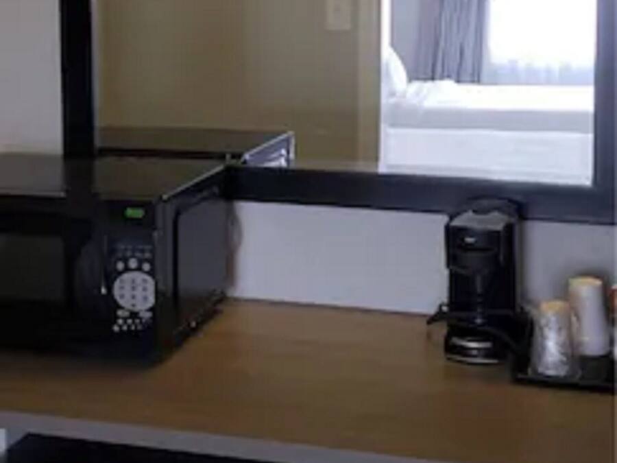A hotel room with a large mirror, a microwave, a coffee maker, and a window with curtains.