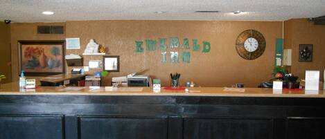 A hotel reception desk with a sign reading "Emerald Inn" and a clock on the wall.