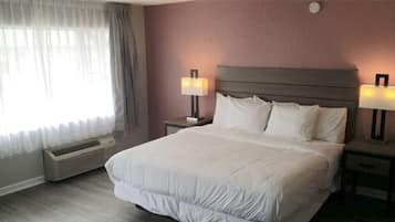 A hotel room with a large bed, two bedside tables with lamps, a window with curtains, and a wall-mounted thermostat.