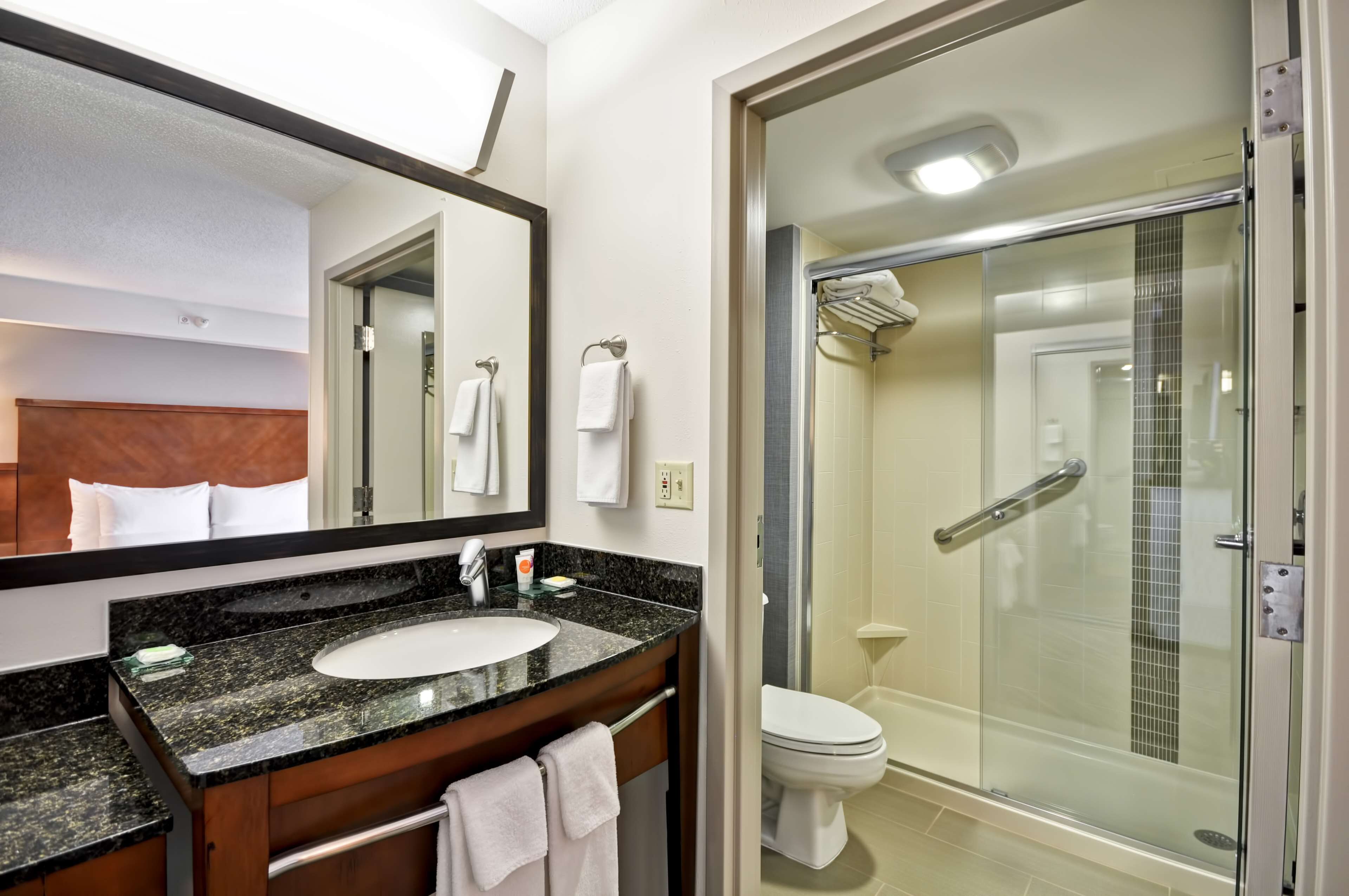 Un baño moderno con lavamanos de granito, un espejo grande, cabina de ducha de vidrio y un inodoro blanco.