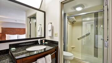 Un baño moderno con lavamanos de granito, un espejo grande, cabina de ducha de vidrio y un inodoro blanco.