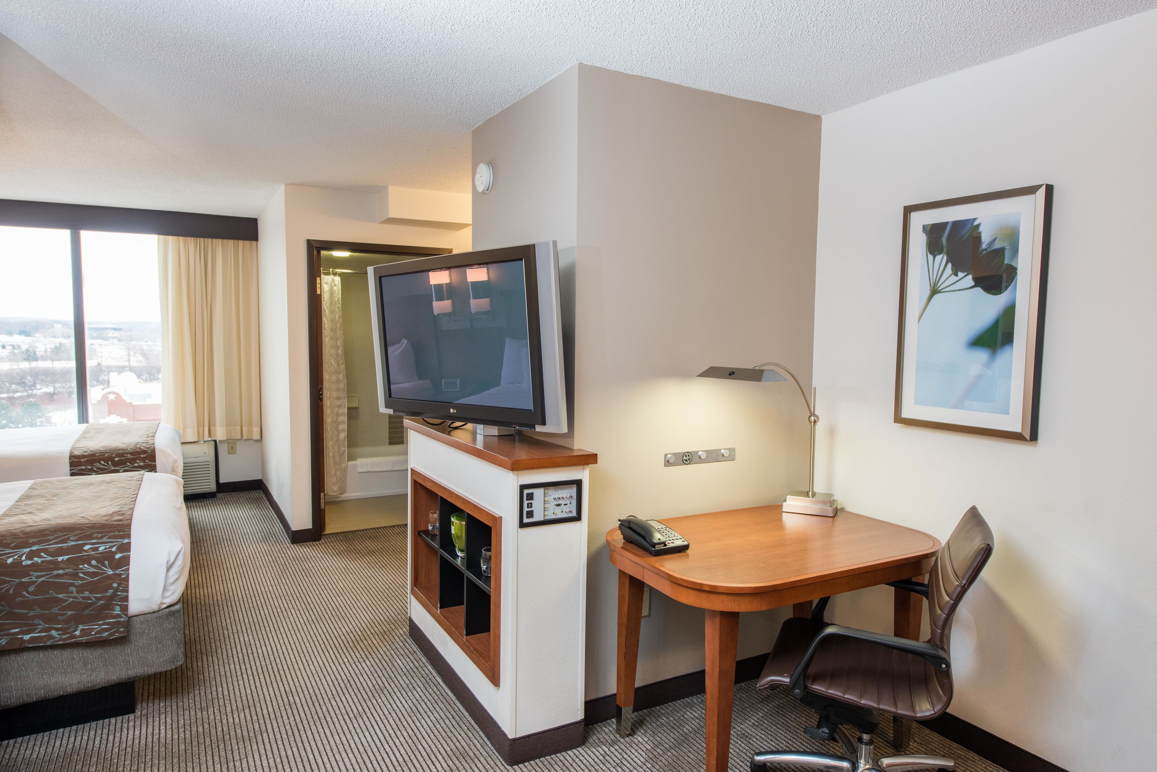 Une chambre d’hôtel comprenant un lit, un bureau avec une chaise, une télévision, une lampe et un tableau encadré au mur.