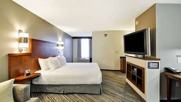 Una habitación de hotel con una cama grande, televisión, escritorio y una silla.