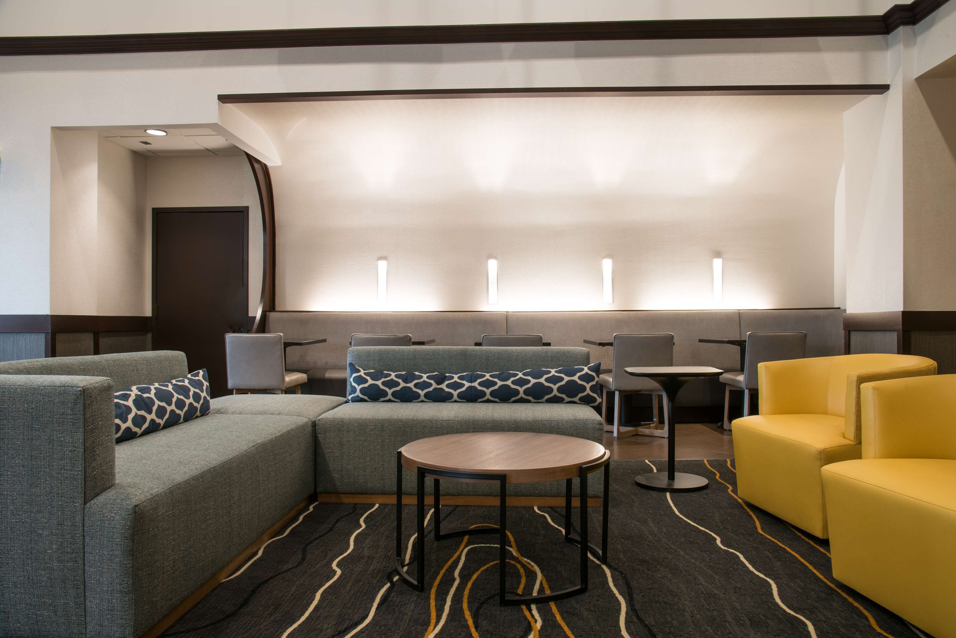 A modern hotel lobby with a sectional sofa, a round table, and yellow armchairs.