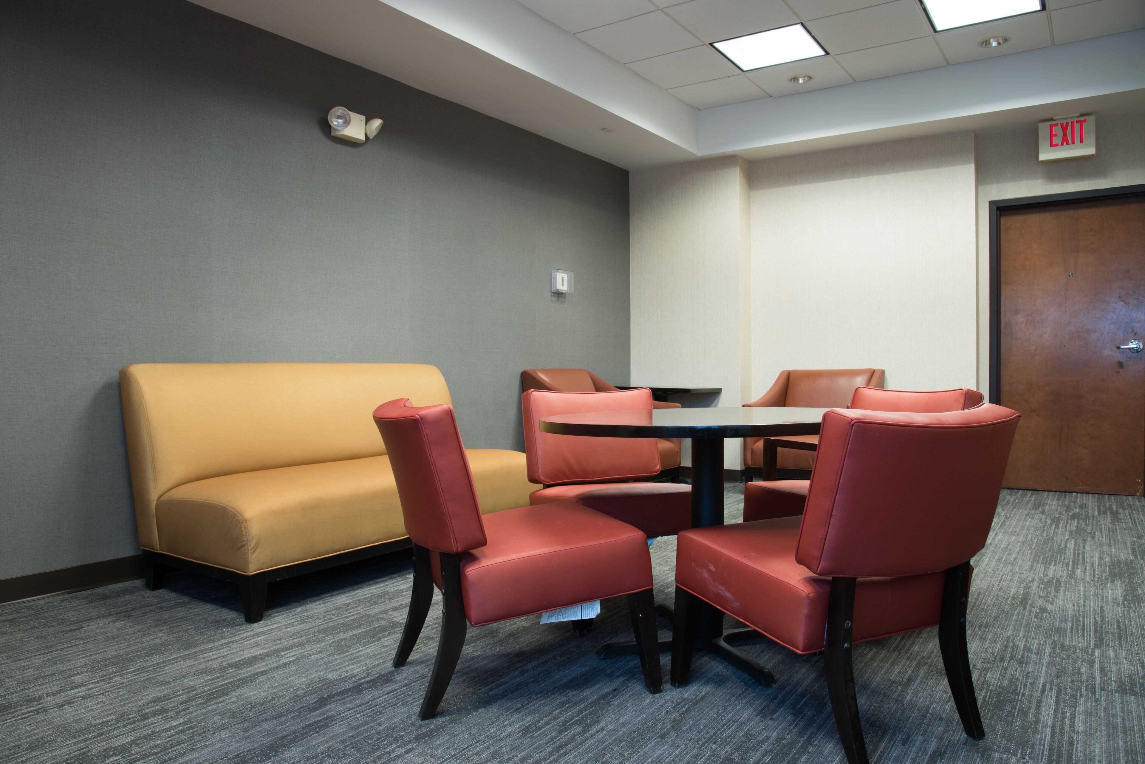 Un salón de conferencias con pared gris, sofá amarillo y sillas rojas alrededor de una mesa.